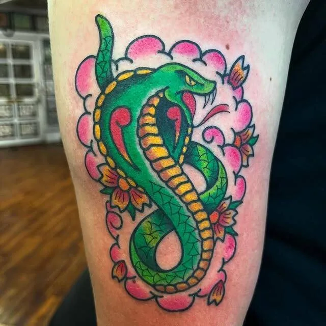 American Traditional color tattoo of a green and gold king cobra rising through a cloud of pink cherry blossoms on the thigh, by Forrest Goodrich at Ohana Tattoo, Waikiki, Hawaii.