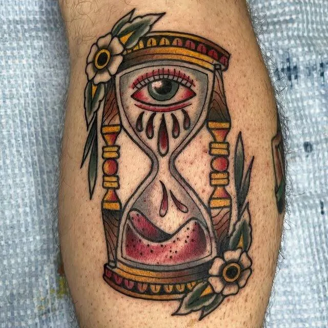 American Traditional hourglass tattoo with a crying eye on top, blood-tinted sand pooling at the bottom and white daisies flanking the wooden frame, on a calf, by Forrest Goodrich at Ohana Tattoo, Waikiki, Hawaii.